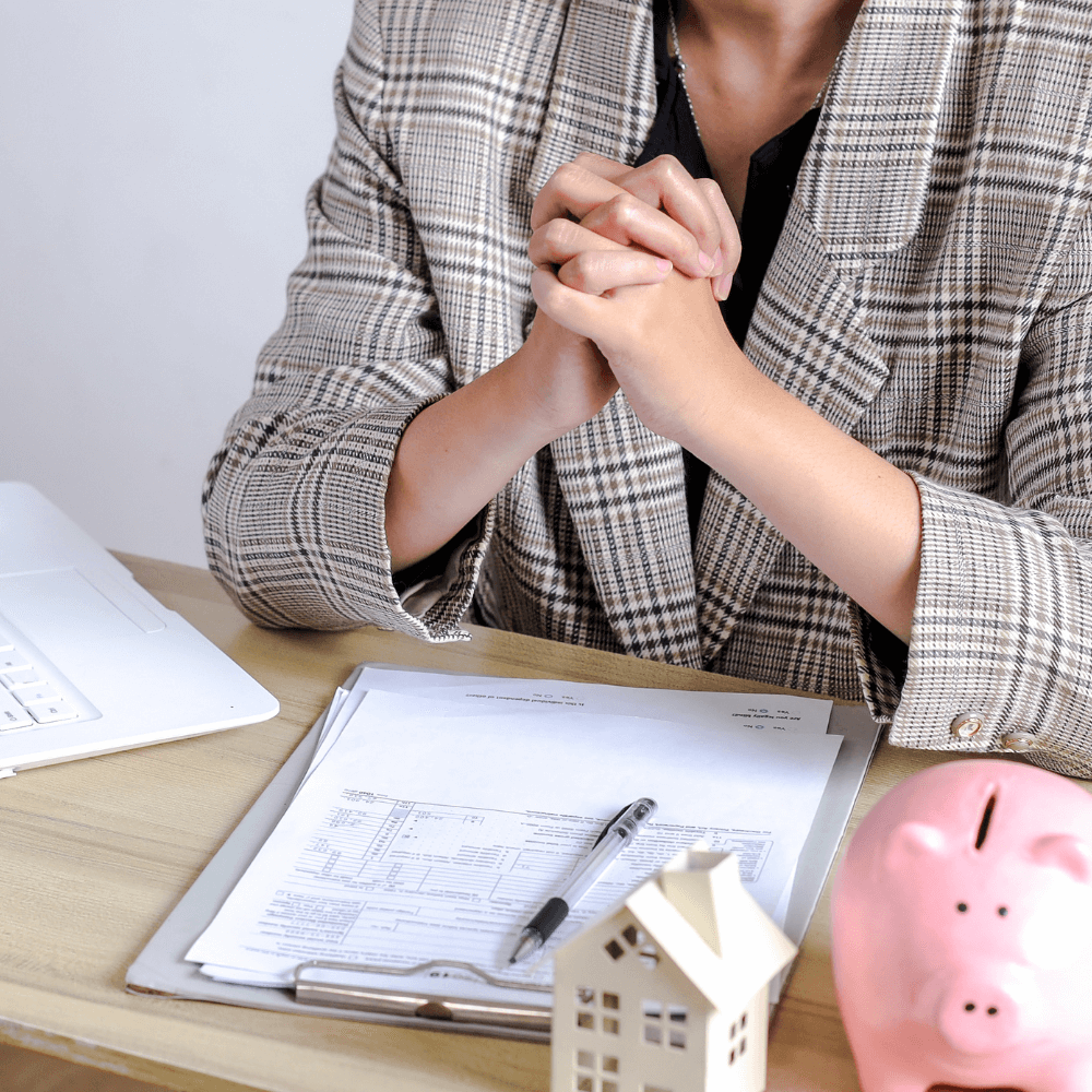 Zoom sur le buste d'une femme assise à un bureau devant un contrat de location avec une figurine d'une petite maison et une tirelire en forme de cochon posés sur le bureau